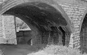 A black and white photograph, through a stone arch
